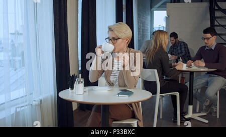 Ritratto di giovane bellissima femmina bere il tè e minuziosamente guardando fuori del coffee shop finestra mentre godendo il suo tempo libero da soli Foto Stock