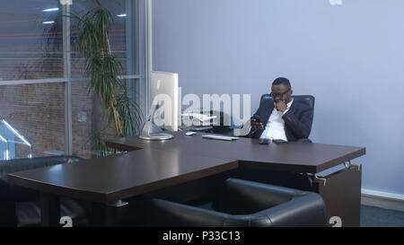 Giovani afro american businessman navigando con lo smartphone, seduta in ufficio Foto Stock