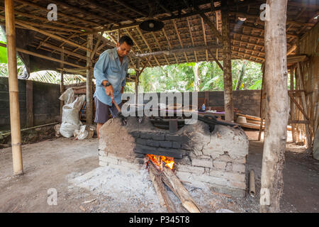 Master girarrosti arrosto manualmente i chicchi di caffè in un legno-sparò stufa vicino Banyuwangi, Java, Indonesia Foto Stock