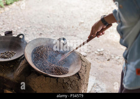 Master girarrosti arrosto manualmente i chicchi di caffè in un legno-sparò stufa vicino Banyuwangi, Java, Indonesia Foto Stock