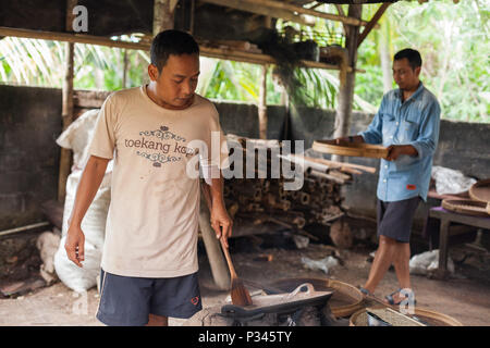 Master girarrosti arrosto manualmente i chicchi di caffè in un legno-sparò stufa vicino Banyuwangi, Java, Indonesia Foto Stock