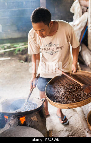 Master girarrosti arrosto manualmente i chicchi di caffè in un legno-sparò stufa vicino Banyuwangi, Java, Indonesia Foto Stock