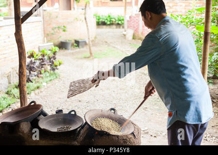 Fanning i chicchi di caffè. Master girarrosti arrosto manualmente i chicchi di caffè in un legno-sparò stufa vicino Banyuwangi, Java, Indonesia Foto Stock