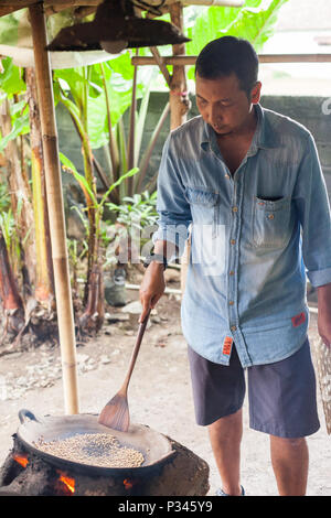 Master girarrosti arrosto manualmente i chicchi di caffè in un legno-sparò stufa vicino Banyuwangi, Java, Indonesia Foto Stock