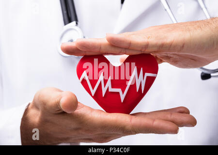 Close-up del medico la mano protegge cuore rosso con Heartbeat Foto Stock