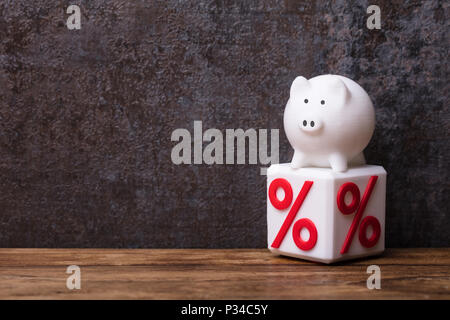 White Piggybank su Blocco cubico con simbolo di percentuale sul tavolato in legno Foto Stock