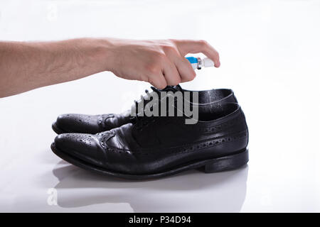 Mano d'uomo deodorante diffusione su scarpe maleodoranti contro uno sfondo bianco Foto Stock