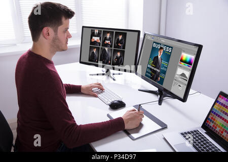 Vista laterale di un Giovane Maschio Designer disegno sulla tavoletta grafica mentre si lavora sul computer Foto Stock