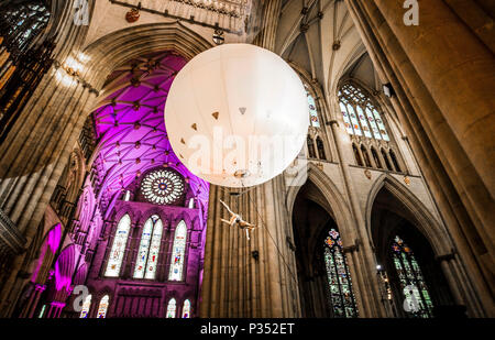 Un acrobat esegue sospendere al di sotto di una gigante palla gonfiabile galleggiante attraverso York Minster la navata, durante una performance di Heliosphere dal sogno del motore. Foto Stock