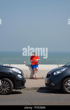 Trattativa, Kent, Regno Unito. Un uomo seduto sulla parete del mare, indossando vestiti di vacanza, in una calda giornata estiva Foto Stock