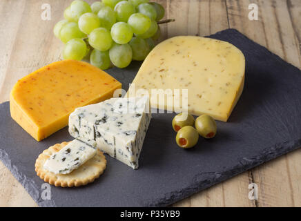 Scheda di formaggio con tre formaggi, gouda con pimento, gouda con semi di cumino e Roquefort formaggio blu vicino sul rustico sfondo di legno Foto Stock