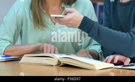 Gli studenti con gli smartphone di scattare una foto della pagina dei libri e rendendo cheat sheet nella biblioteca della scuola Foto Stock