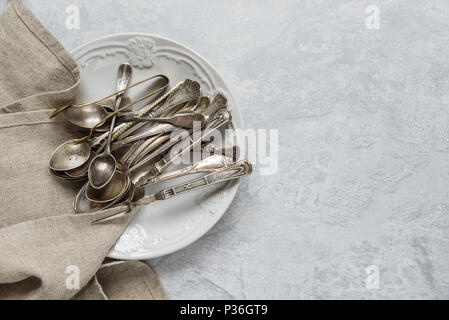Varie argenteria antica su piastra in ceramica su sfondo grigio della superficie in calcestruzzo, con copy-spazio Foto Stock