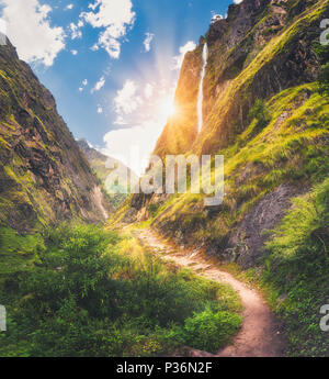 L'Himalayan montagne coperte di verde erba alta cascata, bellissimo percorso, verdi alberi, cielo blu con il giallo del sole e nuvole in Nepal al tramonto. Montagna Foto Stock