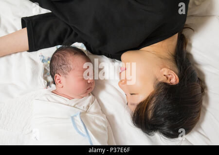 Asian giovane madre e il suo neonato dormendo tranquillamente nel suo letto in camera da letto. Foto Stock