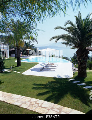 Sentiero lastricato e palme accanto alla piscina a Corfù giardino che si affaccia sul mare Foto Stock