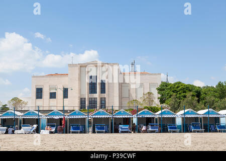 Blue cabanas o dadi di spiaggia su di una spiaggia di sabbia sul Lido di Venezia, Venezia, Veneto, Italia di fronte al Lido Casinò. La gente a prendere il sole, sulla poltrona reclinabile cha Foto Stock