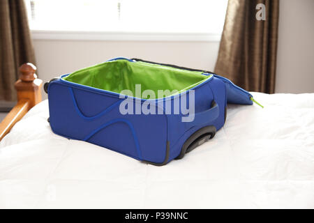 Un blu e verde valigia decompressi siede su un letto, pronto per essere imballato per un'avventura Foto Stock