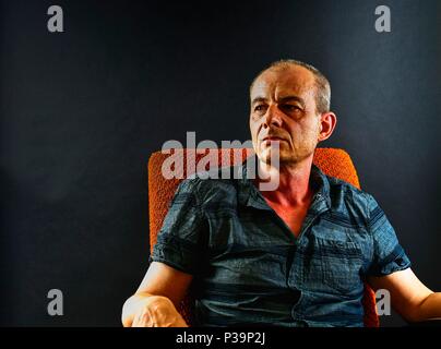 Ritratto di Creative. Uomo di mezza età seduto in poltrona. Ritratto di uomo maturo su sfondo nero Foto Stock