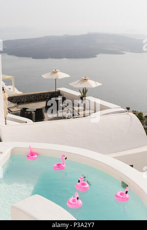 SANTORINI, Grecia - Maggio 2018: rosa fenicottero giocattolo a nuotare in una piscina di lusso vila sull isola di Santorini si affaccia sul vulcano Caldera, Grecia Foto Stock