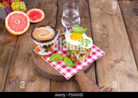 La deliziosa colazione sana. Toast con uova e basilico, fragranti caffè e un bicchiere d'acqua. Pink grapfruit. La cannella sfondo di legno. Foto Stock