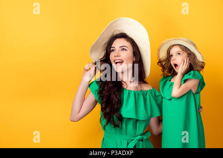 Attraente brunette in hat con larga tesa permanente e la ragazza ha sorpreso con la bocca aperta e la mano sulla guancia su sfondo giallo Foto Stock