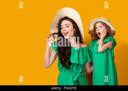 Attraente brunette in hat con larga tesa permanente e la ragazza ha sorpreso con la bocca aperta e la mano sulla guancia su sfondo giallo Foto Stock