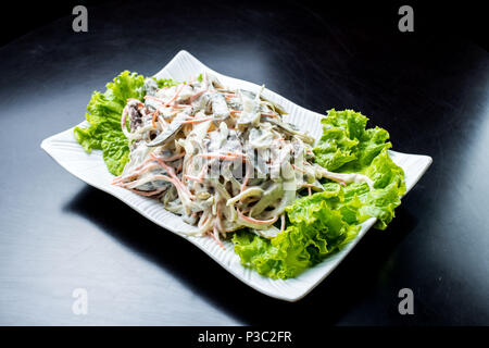 La cucina cinese, con insalata di funghi, carni bovine fritto, sottaceti, lattuga in una piastra bianca su sfondo nero Foto Stock