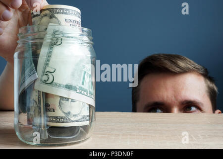 L uomo si prende la banconota dal vaso. Infedeltà finanziaria concetto. Foto Stock