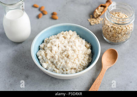 Acciaio tagliati di Avena, fiocchi d'avena porridge nel recipiente. Sana colazione sul cemento grigio sfondo tabella Foto Stock