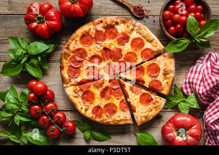 Salsiccia per pizza pizza, pomodori e basilico. Gustosa salsiccia per pizza pizza sul legno rustico sfondo. Vista aerea della pizza italiana Foto Stock