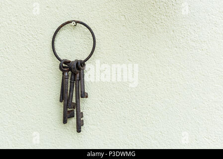Rusty vecchie chiavi appeso su una crema di parete testurizzata. Corroso portachiavi di metallo e chiavi. Foto Stock