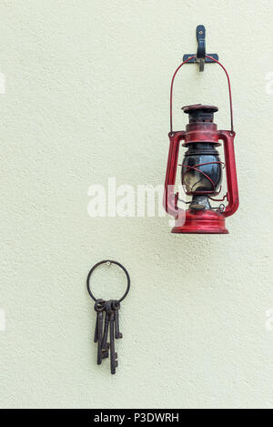 Vecchia lampada di uragano e chiavi appeso a una parete testurizzata. Foto Stock