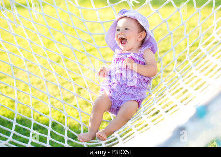 Ritratto di felice ragazza in vacanza. In un contesto di amache, una bambina è seduta in una treccia viola. piccola ragazza ridere, close-up verticale Foto Stock