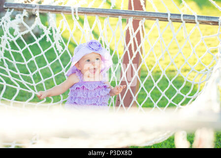 Ritratto di felice ragazza in vacanza. In un contesto di amache, una bambina è seduta in una treccia viola. piccola ragazza ridere, close-up verticale Foto Stock