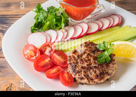 Bistecca tritata scaloppa cucinate alla griglia sulla piastra bianca con assorty mescolare le verdure il Ravanello di pomodori ciliegia fette di cetrioli prezzemolo, limone e salsa ket Foto Stock