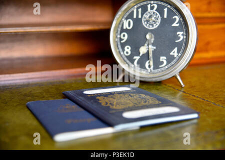 Blu di passaporto britannico e australian passportwith vecchio orologio sveglia su legni antichi scrivania Foto Stock