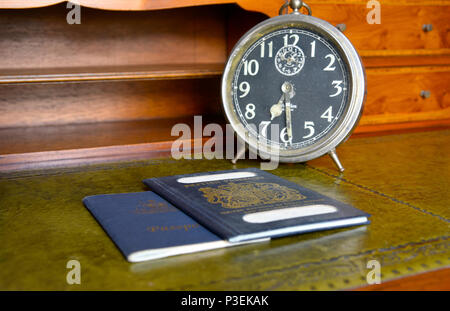 Blu di passaporto britannico e australian passportwith vecchio orologio sveglia su legni antichi scrivania Foto Stock