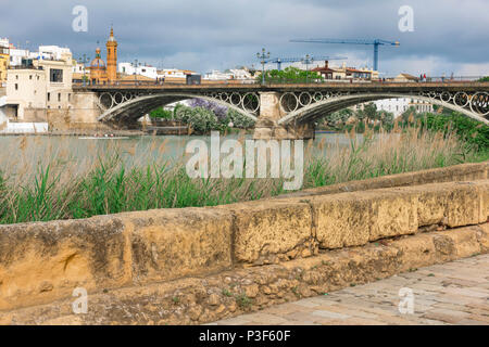 Il fiume di Siviglia, vista attraverso il Rio Guadalquivir verso il Barrio Triana di Siviglia con una sezione della cinta muraria medievale in primo piano, Spagna. Foto Stock