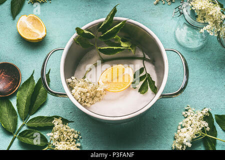 Fiori di sambuco nel recipiente di cottura con zucchero e limone sul tavolo blu sfondo, vista dall'alto. Fiori di sambuco sciroppo o la realizzazione di marmellate Foto Stock