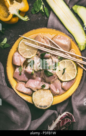 Piastra con carne di pollo, limone , verdure e spiedini di legno sul tavolo da cucina sfondo , vista dall'alto. Preparazione del grill Foto Stock