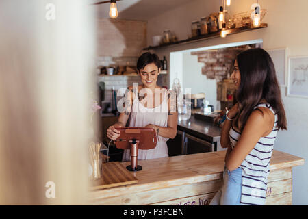 Donna in piedi presso il contatore di fatturazione del suo cafe ad accettare ordini. Donna ordinare del cibo attraverso il contatore in un ristorante. Foto Stock