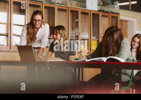 Felice giovane insegnante aiutando una femmina di studente su laptop in aula. Il Professor assistere gli studenti a lezione. Foto Stock