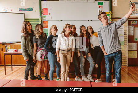 Un gruppo di studenti universitari con insegnante facendo una selfie, giovani con il professore in Aula prendendo selfie con il telefono cellulare. Foto Stock