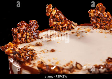 Bianco rotondo torta con caramello e cioccolato riso soffiato su un vassoio rotondo su sfondo nero. Ancora in vita. Close-up Foto Stock