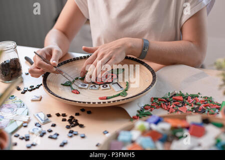 Luogo di lavoro di un mosaico master: mani femminili che definisce un elemento di mosaico sul tavolo. Master stabilisce il mosaico su una piastra Masterclass fatte a mano Foto Stock