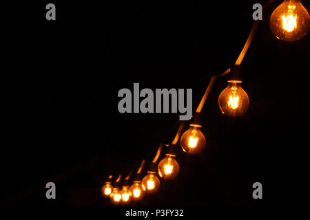 Decorative light bulbs on dark black background and empty space for text Foto Stock