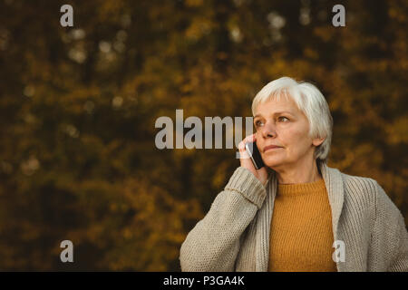 Senior donna utilizzando un telefono intelligente in un parco Foto Stock