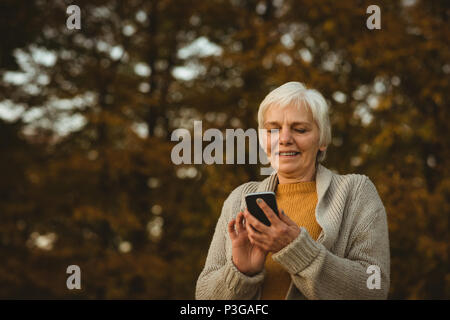 Senior donna utilizzando un telefono intelligente in un parco Foto Stock