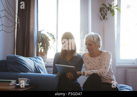 Donna Senior e figlia utilizzando una linguetta mentre si posa sul divano Foto Stock